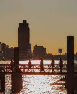 Silhouette buildings by sea against clear sky during sunset