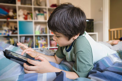 Rear view of boy using mobile phone at home