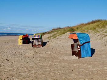 Hooded beach chairs on sand against clear blue sky