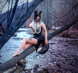 Full length of woman sitting by bare tree in forest