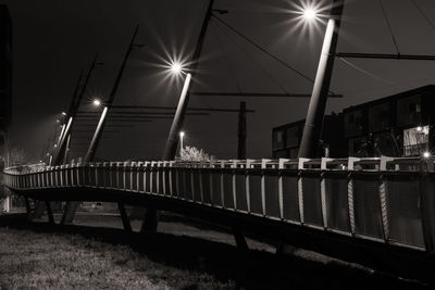 Illuminated street lights against bridge in city at night