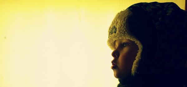 Side view of child wearing hunters cap against clear sky during winter