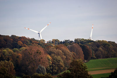 Windmills by forest against sky during autumn