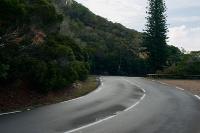 Empty road amidst trees against mountains