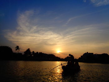 Silhouette people fishing from boat in lake against sky during sunset