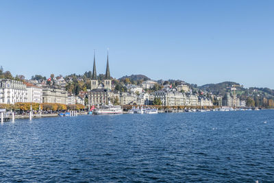 Sailboats in city by buildings against clear sky