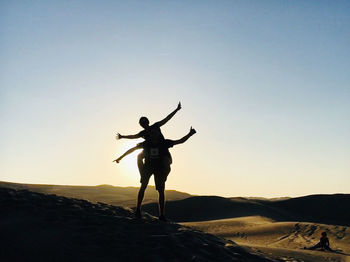 Silhouette person with arms outstretched against sky during sunset