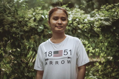 Portrait of smiling young woman standing against trees