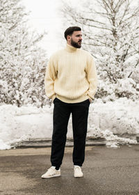 Full length of young man standing against snow covered trees