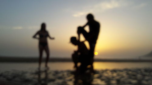 Silhouette people at beach against sky during sunset