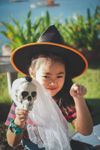 Portrait of girl wearing witch hat holding skull