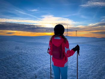 Rear view of woman skier on the slope watching the sunset