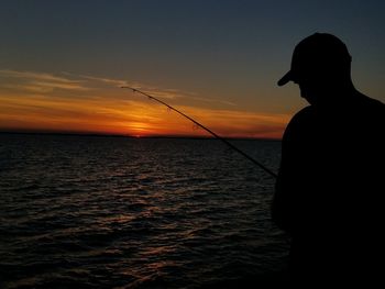 Silhouette mature man fishing in sea against sky during sunset