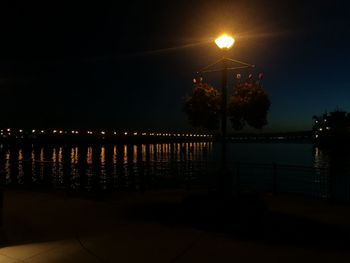 Illuminated street lights by sea against sky at night