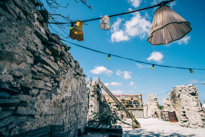 Low angle view of light decorations hanging by stone walls against sky