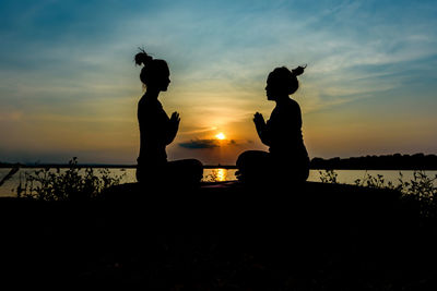 Silhouette people by sea against sky during sunset