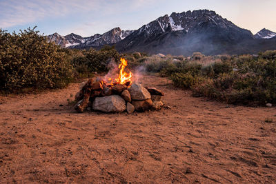 Campsite fire in stone firepit on desert plain at base of mountain