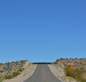 Road amidst land against clear blue sky