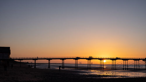 Silhouette bridge over sea against clear sky during sunset