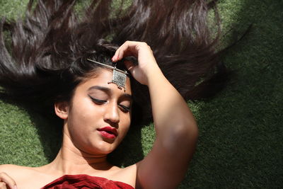 High angle view of young female model wearing jewelry while lying on field