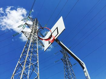 Low angle view of basketball hoop and electricity pylon against blue sky