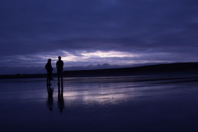 Silhouette couple standing on shore against sky during sunset
