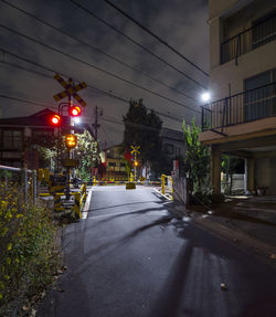 Empty road by illuminated railroad crossing signal against sky at night