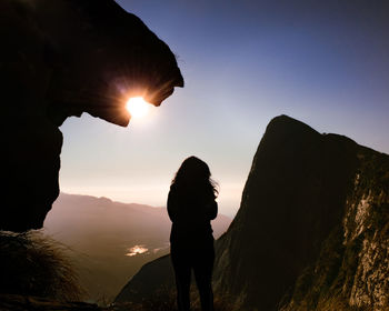 Man standing on rock against sky during sunset