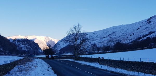 Road amidst snowcapped mountains against clear blue sky