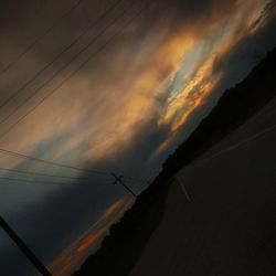 Low angle view of silhouette electricity pylon against dramatic sky