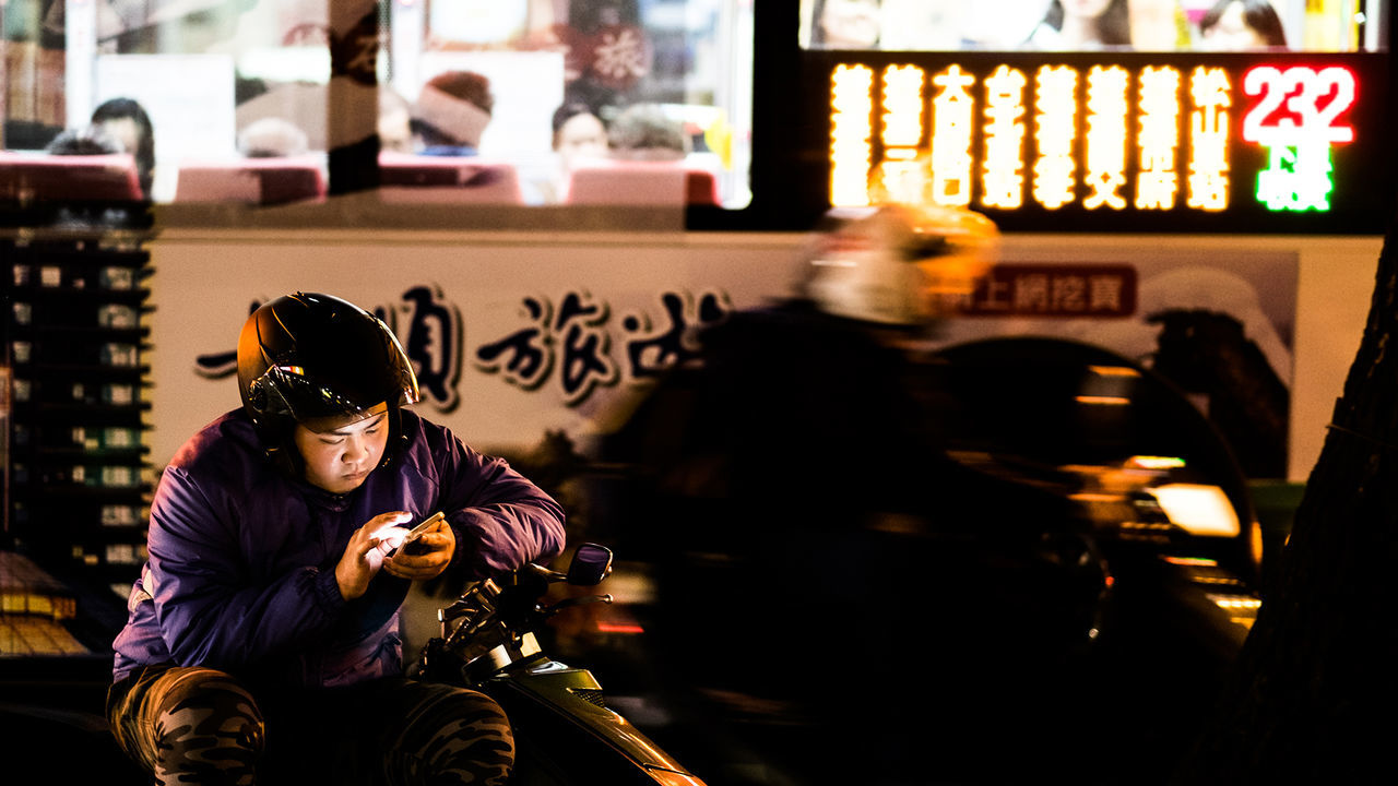 lifestyles, leisure activity, street, person, men, city, illuminated, casual clothing, focus on foreground, rear view, city life, night, incidental people, building exterior, waist up, communication, architecture, three quarter length