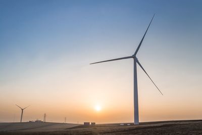 Windmills on landscape against sky during sunset