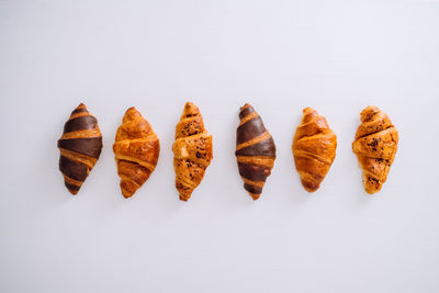Flat lay of several delicious brown and chocolate croissants laid out in a line on a white table	
