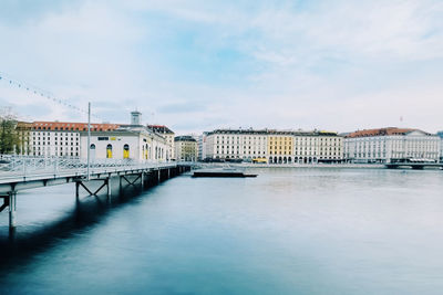 Bridge over river by buildings against sky