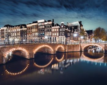 Illuminated bridge over river in city against sky at night