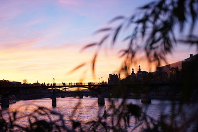 Silhouette buildings by river against sky at sunset