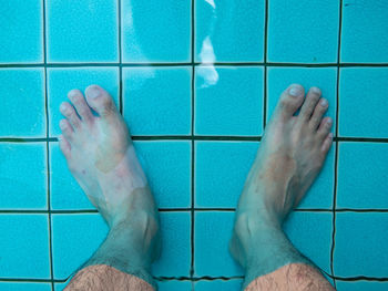 Low section of man standing on tiled floor in swimming pool