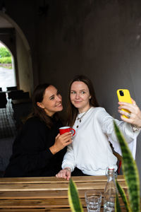 Two women friends have fun outdoors in cafe and take a selfie on a smartphone