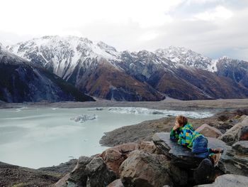 Boy lying on rock by lake against mountain range