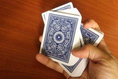 Cropped hands of person holding playing cards on wooden table