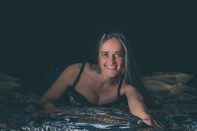 Portrait of woman smiling while lying on bed against black background
