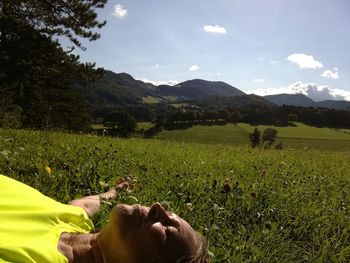 Low section of person relaxing on field against sky