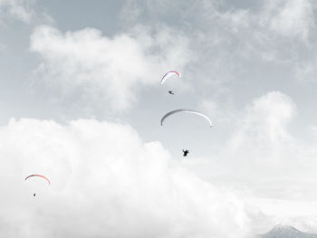 Low angle view of people paragliding against sky