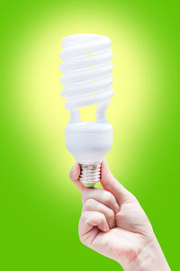 Cropped image of hand holding light bulb against green background