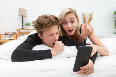 Couple using mobile phone on bed at home