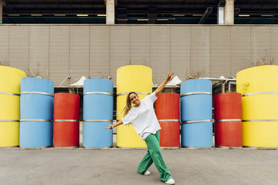 Happy young woman with arms outstretched dancing in front of concrete pipes