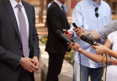 Cropped hands holding microphones towards businessman