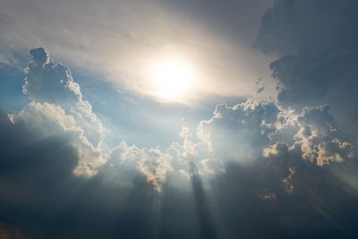 Low angle view of sunlight streaming through clouds