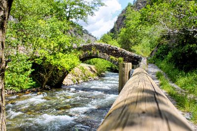 Arch footbridge over river against tree mountains