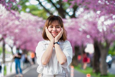 Portrait of woman with pink flower standing against trees